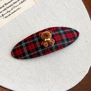 Close-up of red and black plaid fabric hair clip with a cute brown flocked bear ornament