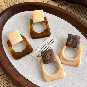 Detail view of geometric square drop earrings with wood and resin textures in a retro style