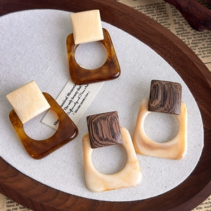 Macro detail of French retro resin and wood square geometric earrings on a canvas background