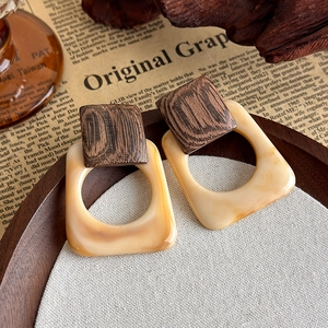 Detail of square geometric resin earrings with dark wood texture on a textured fabric surface