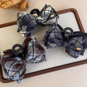 Close-up of fabric plaid bow hair claw with gold LOVE metal emblem and premium woven texture