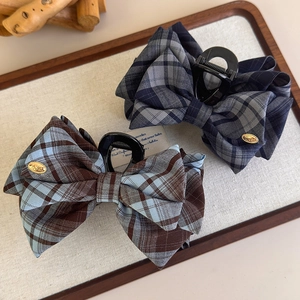 Detail of British style plaid bow hair claws with gold metal tags on linen background