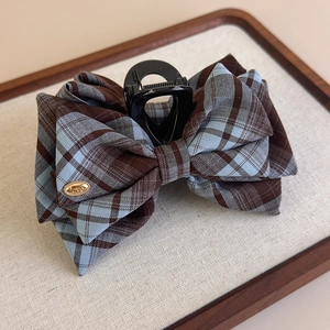 Detail of checkered plaid bow hair claw with gold Love metal tag on beige tray
