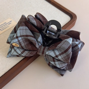 Detail of plaid bow hair claw clip with golden metal accent and sturdy black resin teeth