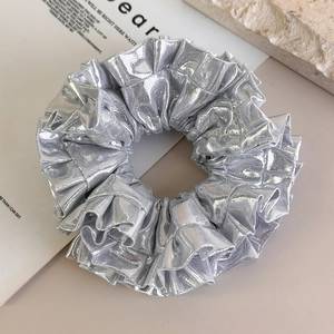 Dettaglio di scrunchie argento metallizzato con tessuto a pieghe lucido e texture