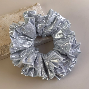 Dettaglio ravvicinato di un elastico per capelli argento metallizzato con tessuto plissettato