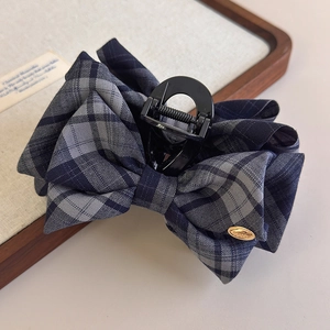 Detailed close-up of grey and navy plaid bow hair claw with elegant golden metal logo