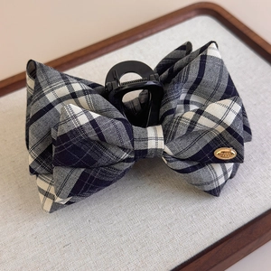 Detail view of a plaid bow hair claw clip with a gold LOVE metal tag on a wooden tray