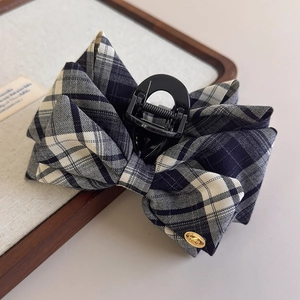 Detail of a black and white plaid bow hair claw clip with a golden metallic accent