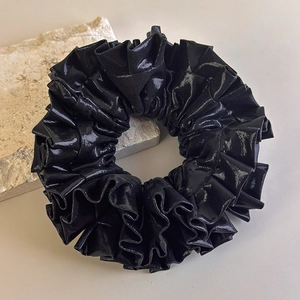 Dettaglio ravvicinato di un elastico per capelli plissettato nero metallizzato su pietra