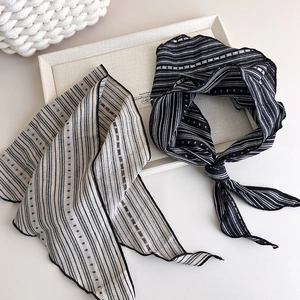 Detail of retro striped cotton scarves in black and beige displayed on a texture tray
