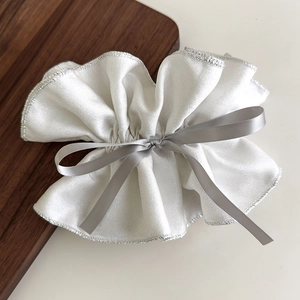 Nahaufnahme eines weißen gerafften Scrunchie mit Silberkante und Satin-Schleifen-Detail