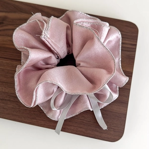 Detail eines rosa perlmuttfarbenen Haargummis mit Silberrand und weißer Satinschleife