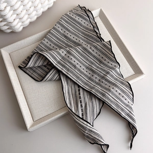 Detailed view of striped beige fabric neck scarf with black dots on a textured tray