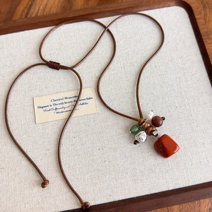 Détail du collier ethnique long avec pendentif jaspe rouge et perles bois sur plateau lin