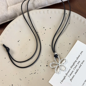 Close-up of silver hollow flower pendant with black wax cord on a textured plate