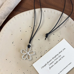 Close-up of silver hollow flower pendant with matte texture on black cord necklace