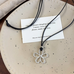 Close-up of silver hollow flower pendant on black cord over a ceramic tray