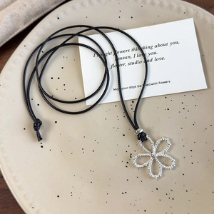 Detail shot of silver hollow flower pendant with black waxed cord on ceramic tray