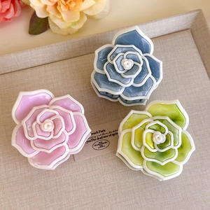 Dettaglio di tre mollette per capelli a camelia in acetato nei colori rosa, blu e verde