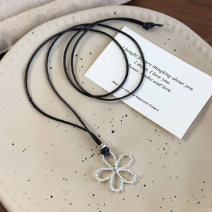Close-up of a silver hollow flower pendant on a black adjustable cord over a ceramic plate