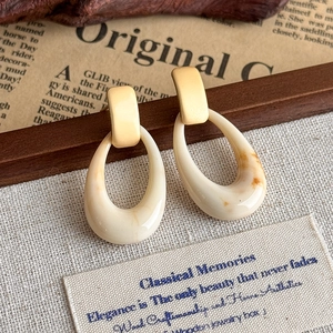Dettaglio di orecchini ovali in resina con trama ambra crema su uno sfondo vintage