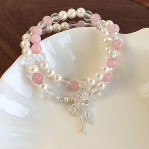 Double-layer pearl and pink bead bracelet with silver bow pendant on ceramic tray