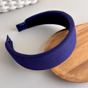 Detail of dark purple knitted padded headband showing ribbed texture on a wooden tray