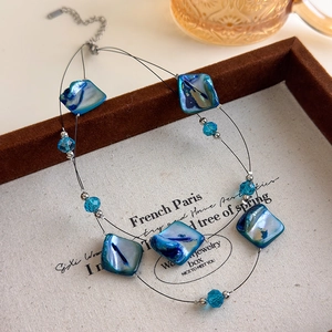 Close-up of double-layer shell necklace with blue crystal beads on textured linen tray
