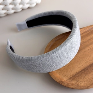 Close-up of light gray knitted thick headband with soft texture on a wooden tray
