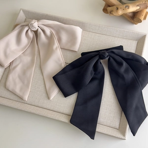 Elegant large satin bow hair clips in black and cream beige on a grey textured display tray