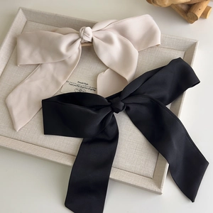 Detailed macro view of elegant black and cream satin bow hair clips on a textured tray