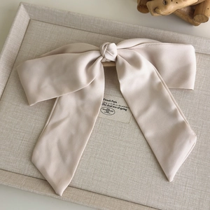 Detail of elegant beige satin bow hair clip on textured display tray in French style