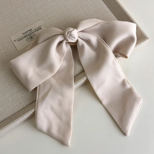 Elegant beige chiffon bow hair clip with long ribbons on a decorative tray