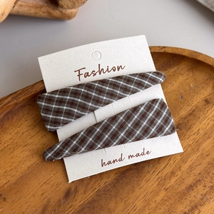Macro shot of two brown and cream plaid fabric hair clips on a fashion display card