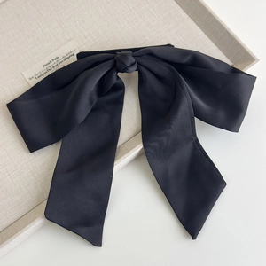 Detailed macro view of an elegant large black satin bow hair clip on a textured cream tray