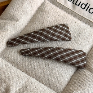 Detail of classic brown plaid fabric hair clips set on a soft quilted fabric background