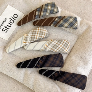 Close-up showing six vintage plaid fabric hair clips with fringe on a soft texture mat
