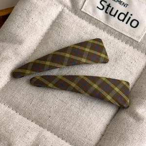 Detailed close-up of vintage plaid triangular hair clips in dark green scottish fabric