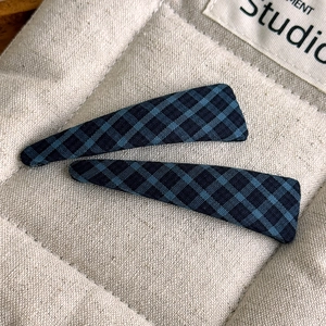 Macro view of two blue and black plaid triangle hair clips on quilted fabric background