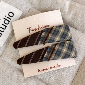 Close-up of handmade plaid and striped fabric BB clips with fringe details on a card