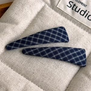 Detail of dark blue plaid fabric hair clips with woven texture on a beige background