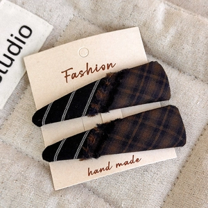 Detail shot of plaid and striped fabric hair clips with fringe and plush on display card