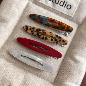 Close-up of four elegant acetate oval hair clips in amber, leopard, red and marble textures