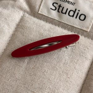Macro shot of matte dark red acetate oval hair clip on textured beige linen background