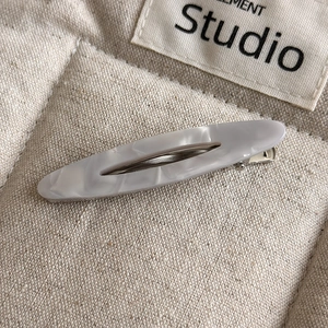 Close-up of an oval acetate hair clip with a marble texture on a soft fabric background