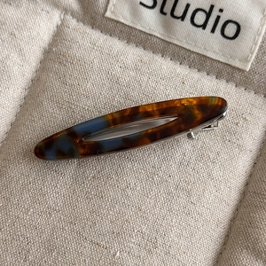 Close-up of acetic acid oval hair clip with brown and blue tortoiseshell pattern