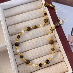 Détail d'un collier de pierres œil de tigre et perles blanches sur velours beige