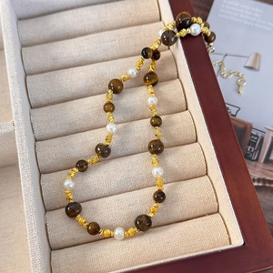 Détail du collier de perles en œil de tigre et perles blanches dans son coffret à bijoux