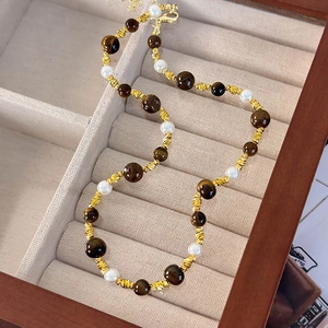 Gros plan du collier en œil de tigre et perles avec entretoises dorées dans une boîte